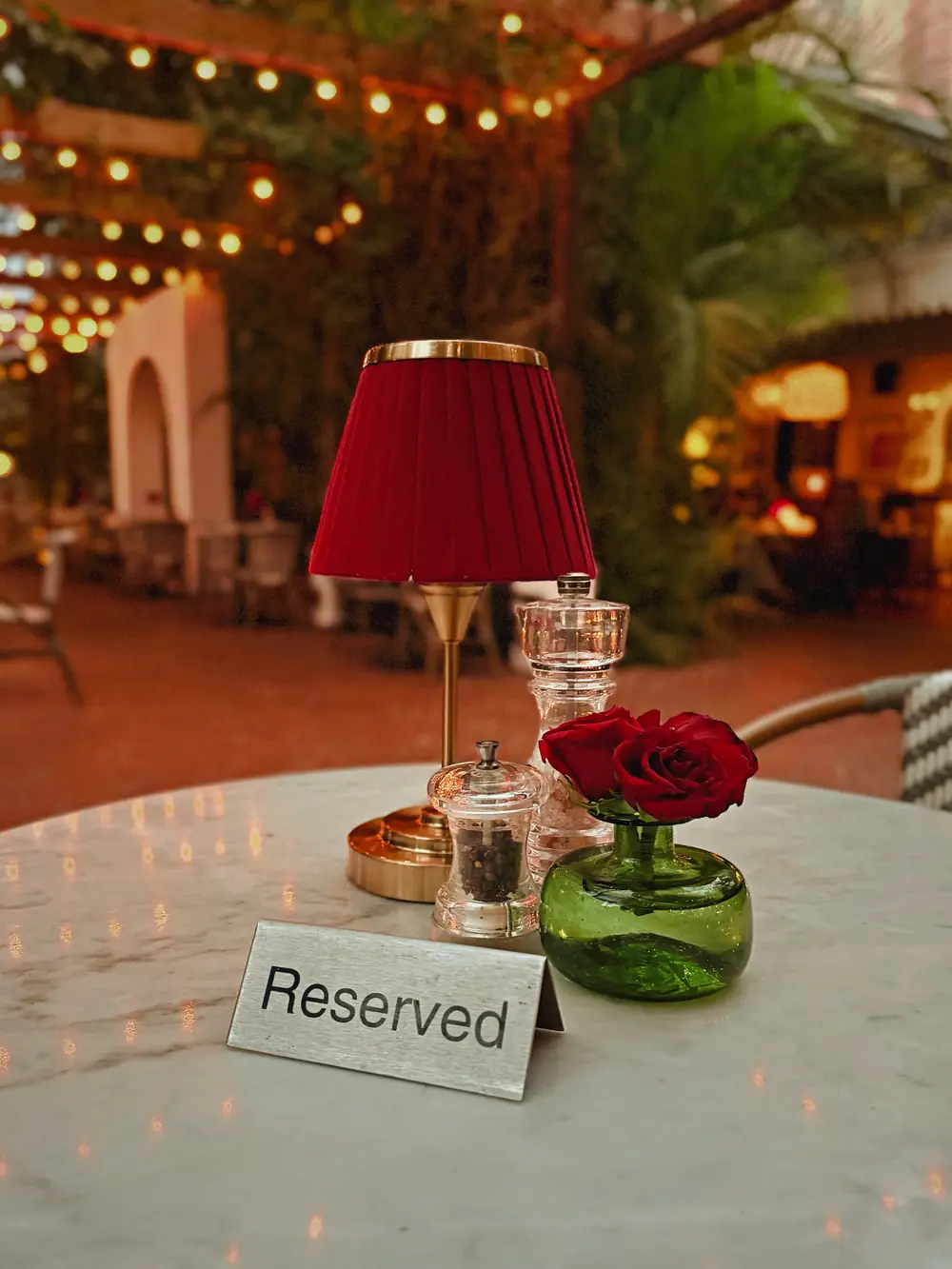 A marble table set with a red lamp, a single red rose and a Reserved sign
